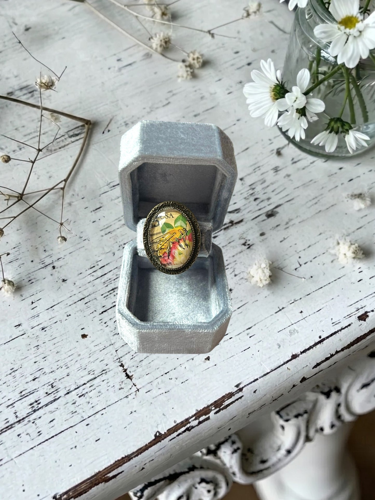Anello artigianale italiano con ape su portanelli azzurro davanti a una finestra, montatura ovale color
bronzo