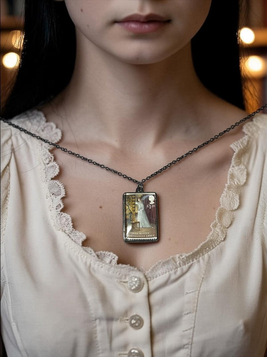 Il ciondolo rettangolare in metallo scuro della collana Jane Austen L'Abbazia di Northanger, con il francobollo Royal Mail del 2013 incastonato al centro, indossato su un busto.