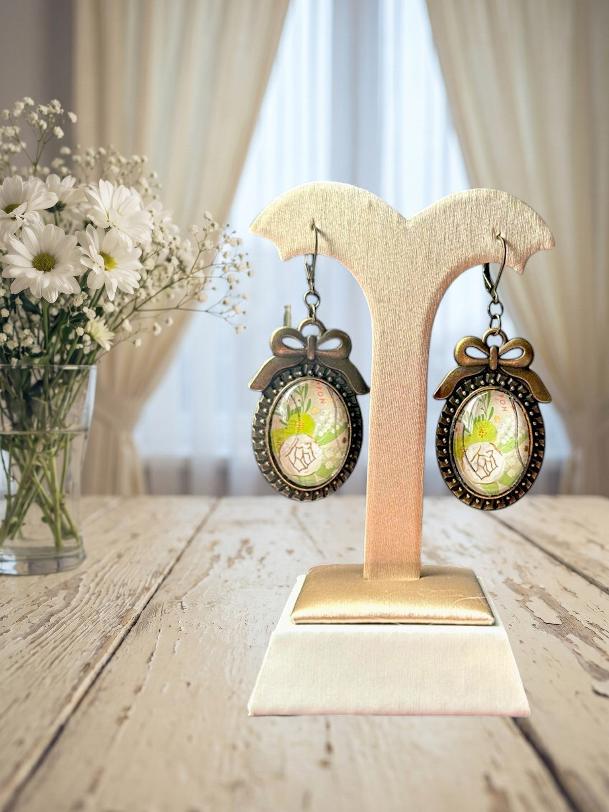 Orecchini artigianali italiani con fiori bianchi e mughetto su portaorecchini beige-oro davanti a una
finestra