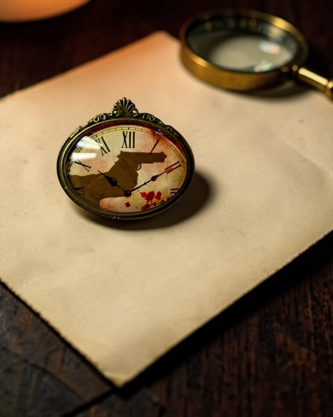 Spilla ovale Lady Nostalgia con francobollo di Agatha Christie: quadrante d'orologio, sagoma di rivoltella e gocce di sangue.