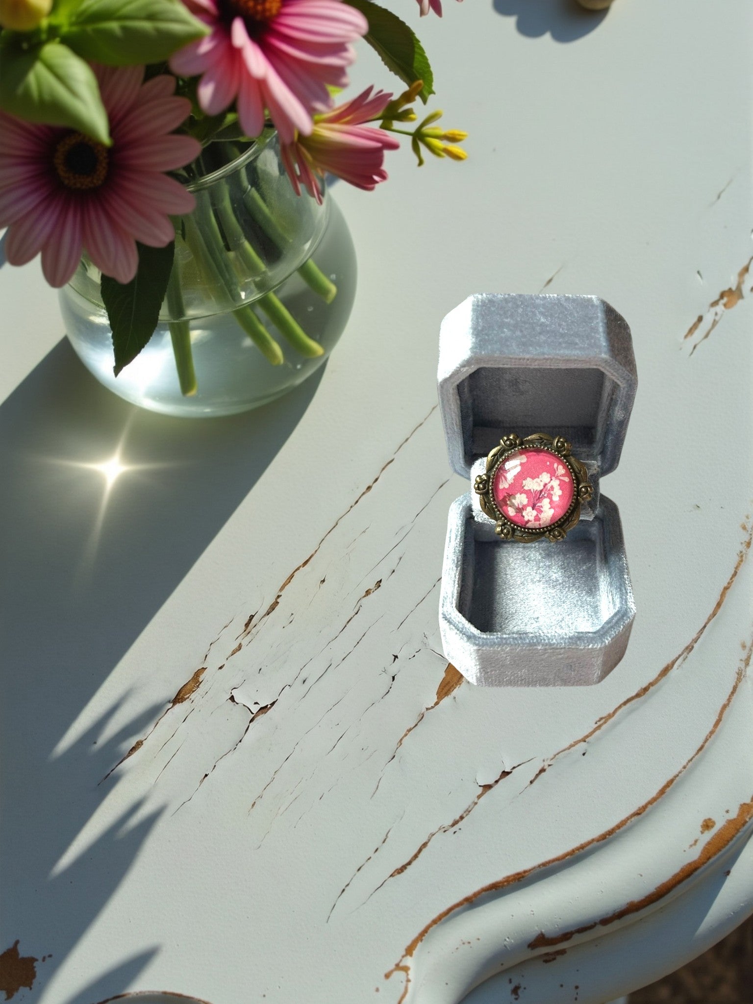 Anello artigianale italiano con fiori di ciliegio su portanelli azzurro davanti a una finestra, montatura
bronzo