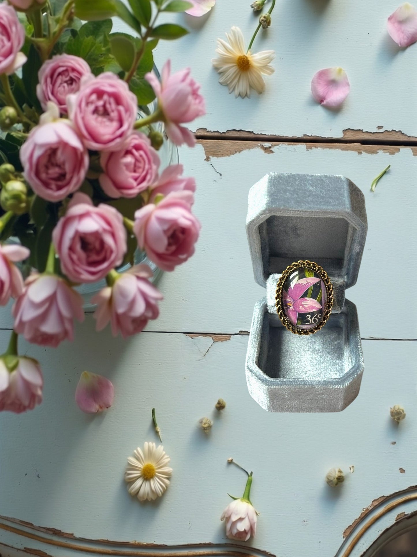 Anello artigianale italiano con orchidea viola su portanelli azzurro davanti a una finestra, montatura
ovale color oro