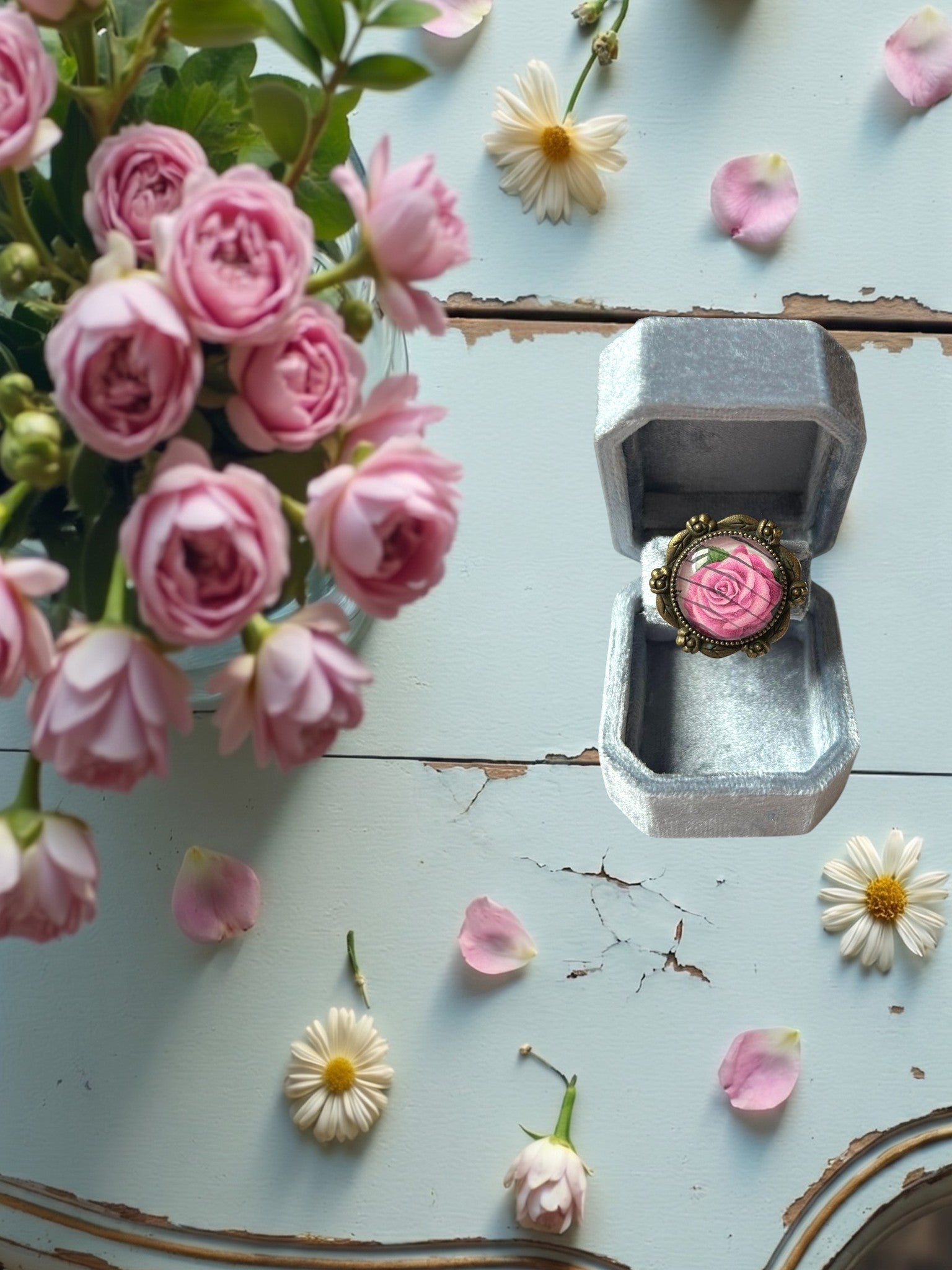 Anello artigianale italiano con rosa rosa su portanelli azzurro davanti a una finestra, montatura bronzo a
roselline