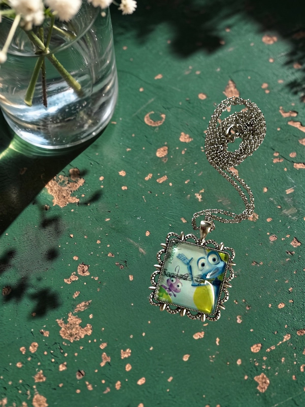 Ciondolo quadrato artigianale con francobollo A Bug's Life su tavolo verde, montatura argentata, realizzato in Italia