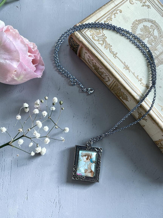 Collana con ciondolo rettangolare argentato e francobollo d'epoca di André, personaggio di Lady Oscar, su libro antico