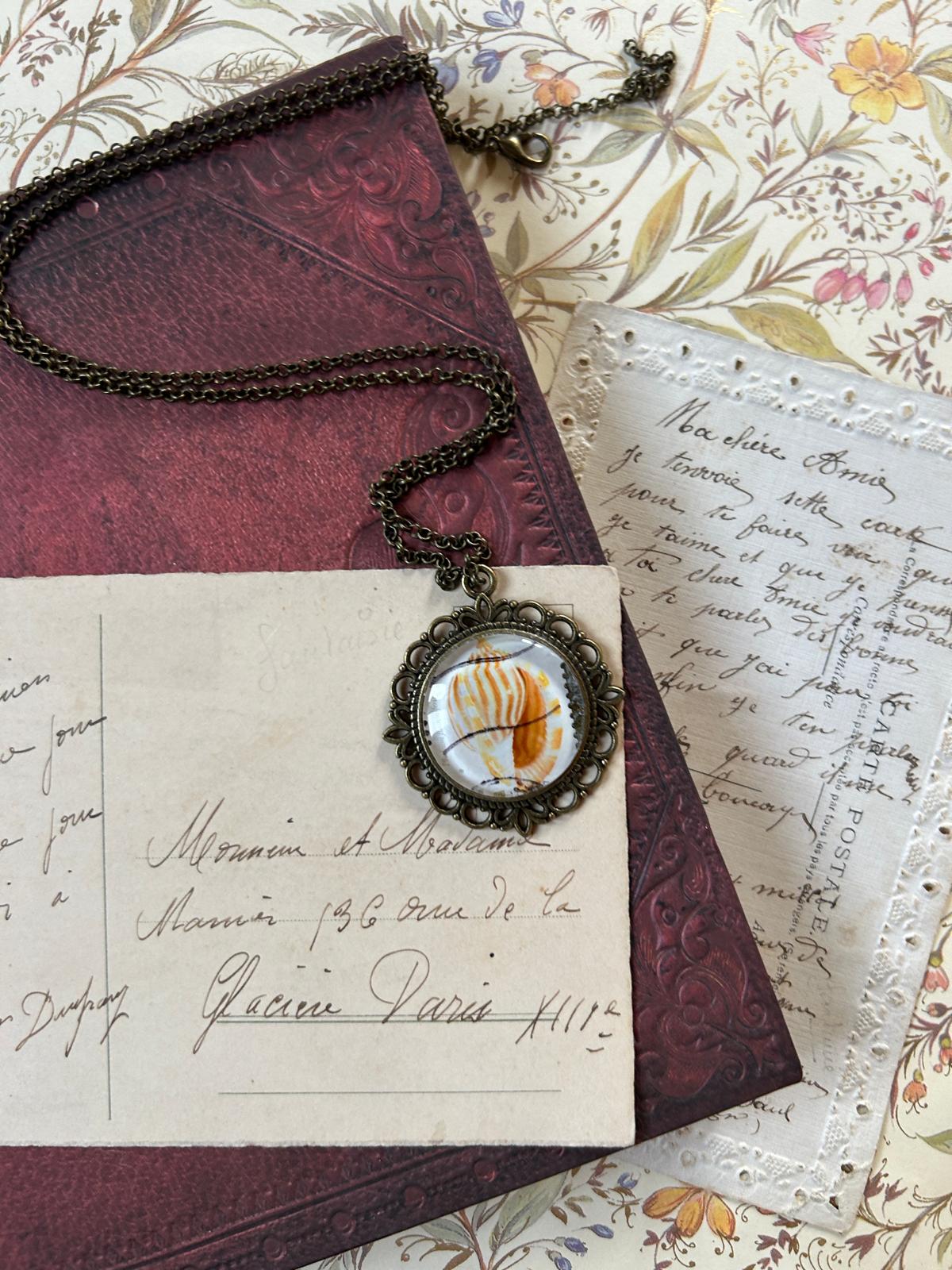 Collana artigianale fatta in Italia con ciondolo a conchiglia da francobollo giapponese, posata su una lettera manoscritta