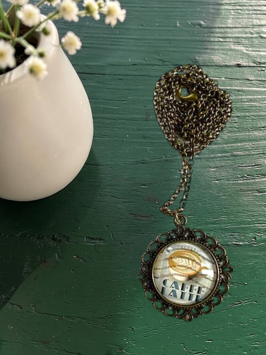 Ciondolo tondo artigianale italiano con francobollo caffè latte su tavolo verde, cornice bronzo