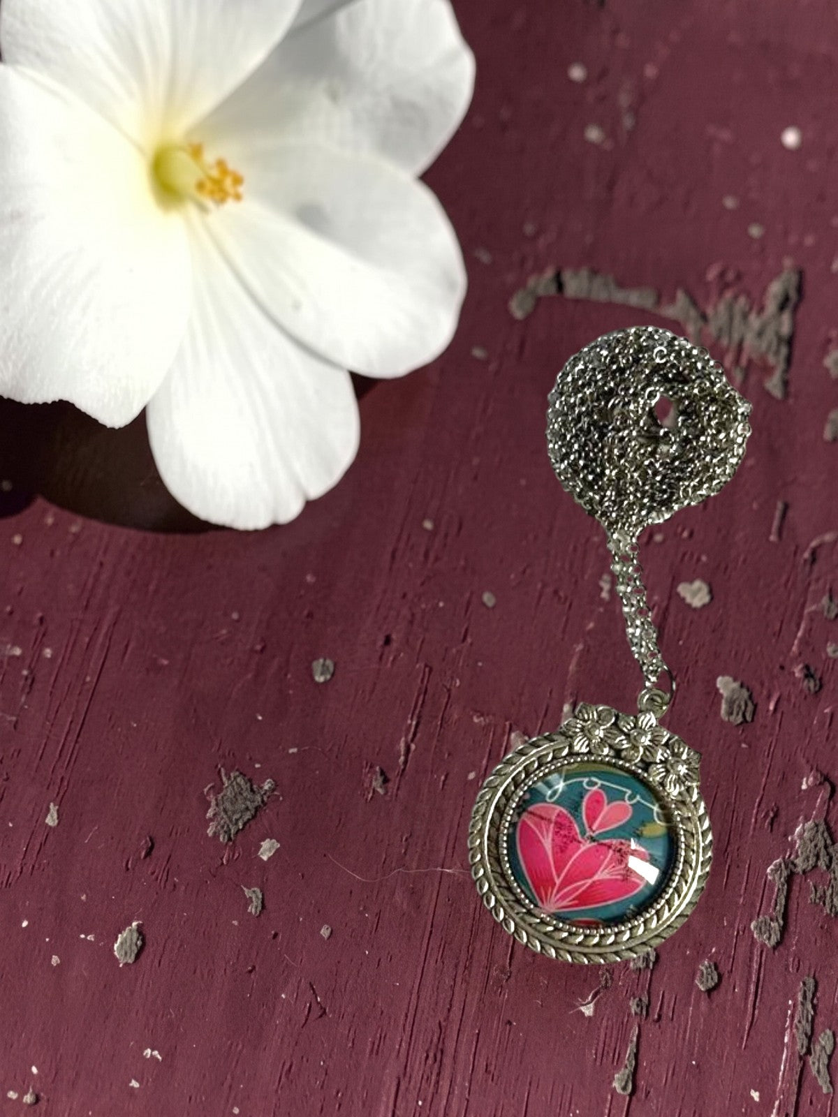 Ciondolo tondo artigianale italiano con francobollo di un cuore rosa dell'amore su tavolo bordeaux, cornice argentata