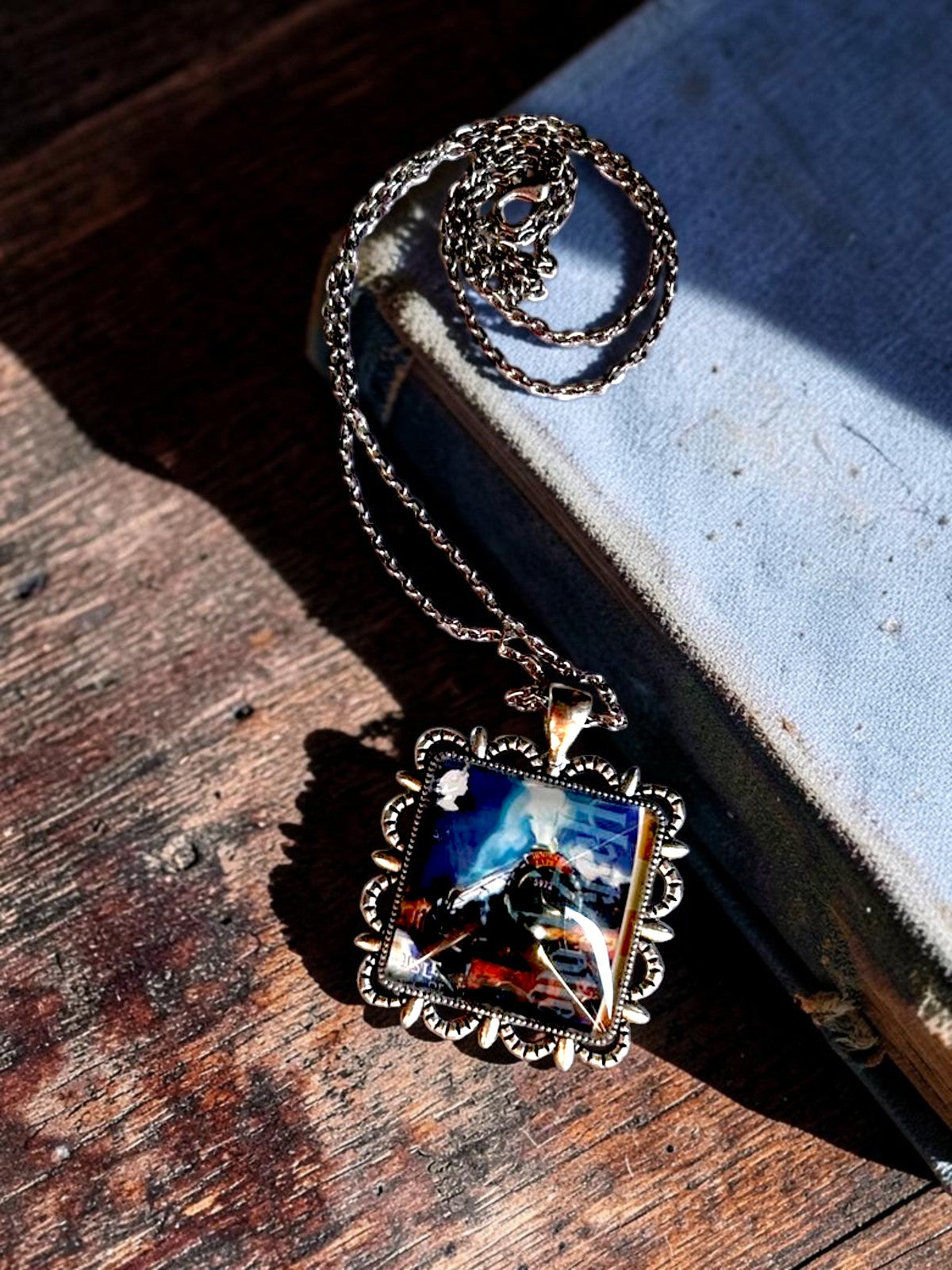 Collana artigianale italiana con il treno di Hogwarts da francobollo dell'Isola di Man, posata su un libro antico