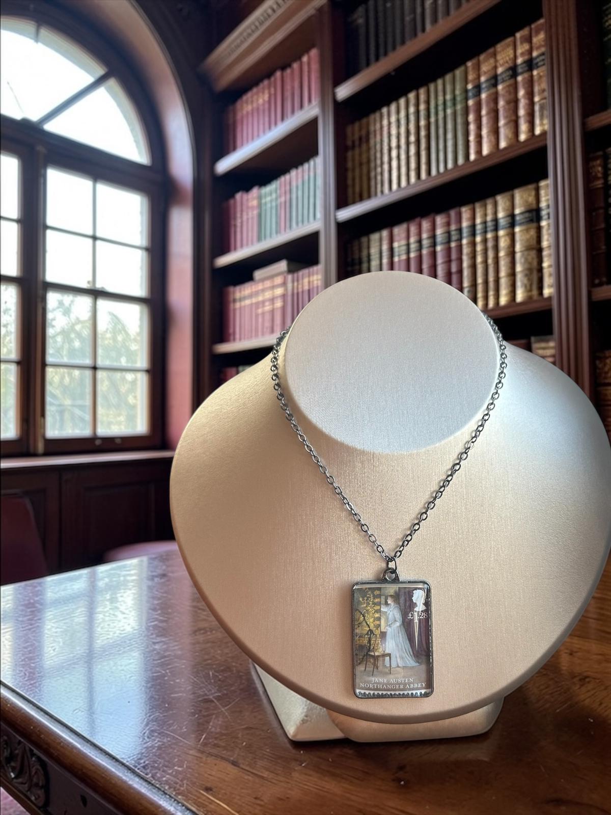 Collana Jane Austen con il francobollo Royal Mail del 2013 dedicato a L'Abbazia di Northanger, illustrato da Angela Barrett, incastonato in una montatura rettangolare di metallo scuro. La collana è indossata su un busto.