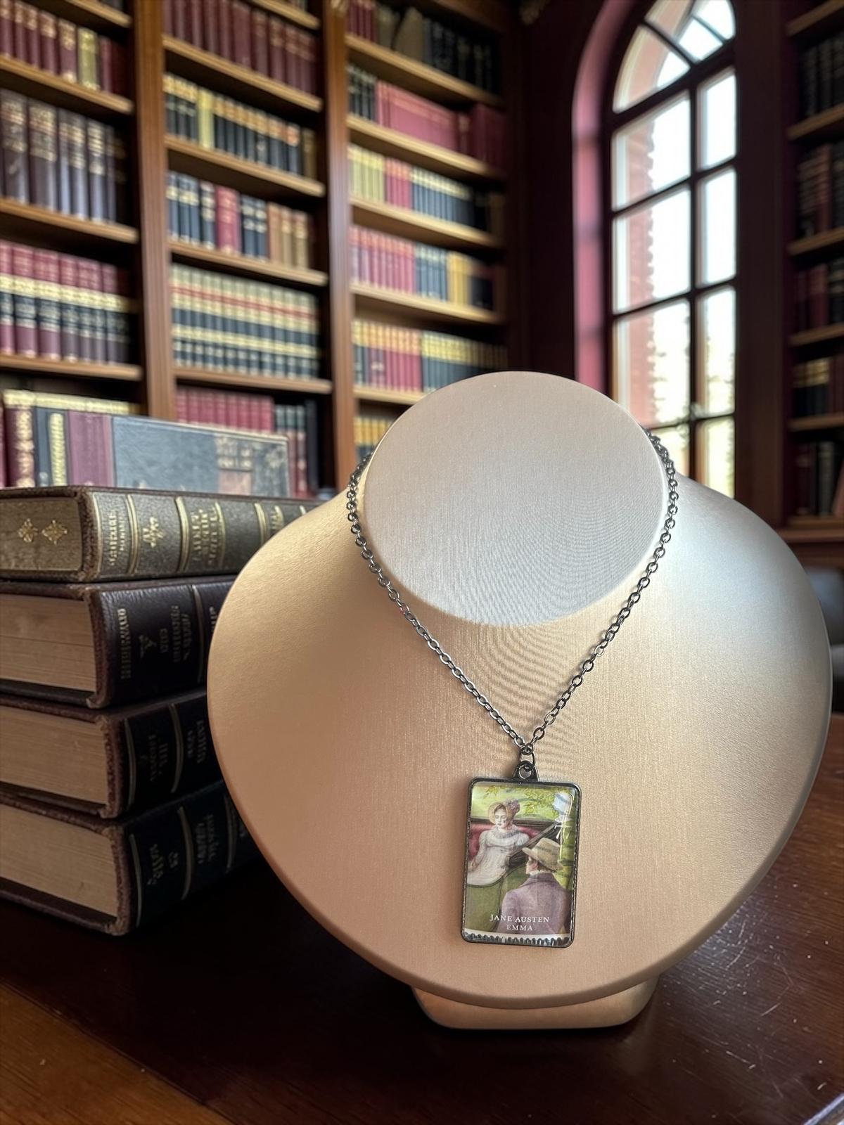 Collana Jane Austen con il francobollo Royal Mail del 2013 dedicato a Emma, illustrato da Angela Barrett, incastonato in una montatura rettangolare di metallo scuro. La collana è indossata su un busto.