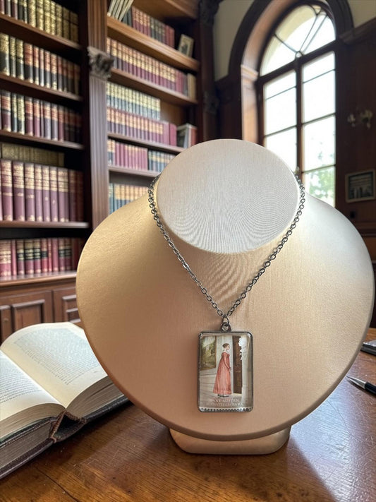 Il ciondolo rettangolare in metallo scuro della collana Jane Austen Mansfield Park, con il francobollo Royal Mail del 2013 incastonato al centro, indossato su un busto.