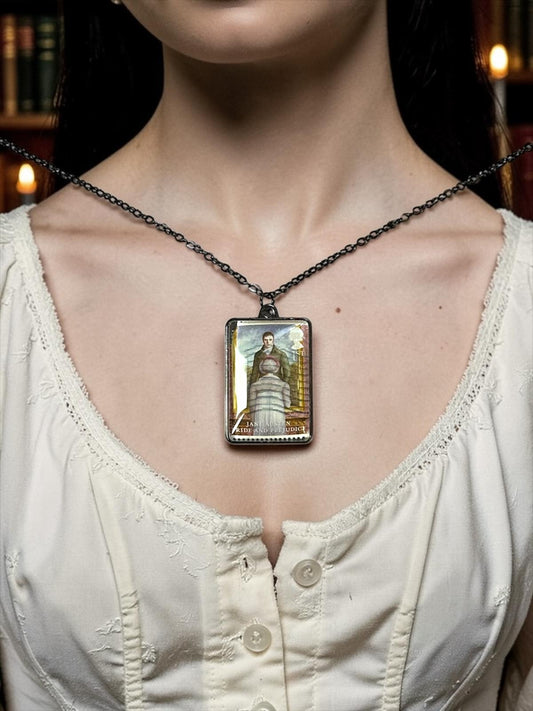 Collana Jane Austen con il francobollo Royal Mail del 2013 dedicato a Orgoglio e Pregiudizio, illustrato da Angela Barrett, incastonato in una montatura rettangolare di metallo scuro. La collana è indossata su un busto.