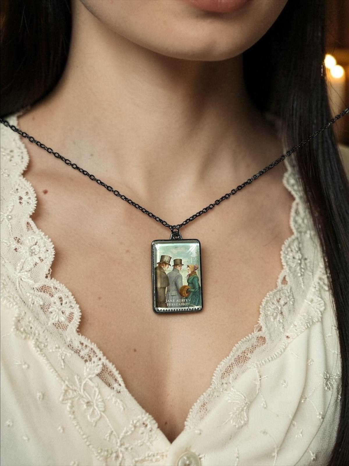 Il ciondolo rettangolare in metallo scuro della collana Jane Austen Persuasione, con il francobollo Royal Mail del 2013 incastonato al centro, indossato su un busto.