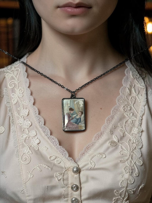 Il ciondolo rettangolare in metallo scuro della collana Jane Austen Ragione e Sentimento, con il francobollo Royal Mail del 2013 incastonato al centro, indossato su un busto.