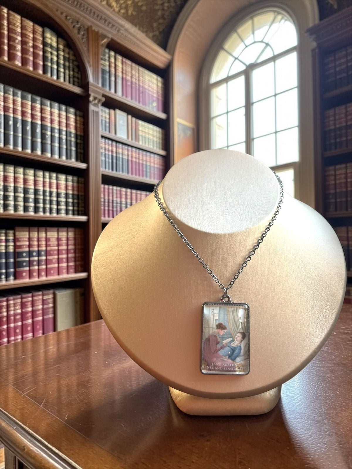 Collana Jane Austen con il francobollo Royal Mail del 2013 dedicato a Ragione e Sentimento, illustrato da Angela Barrett, incastonato in una montatura rettangolare di metallo scuro. La collana è indossata su un busto.