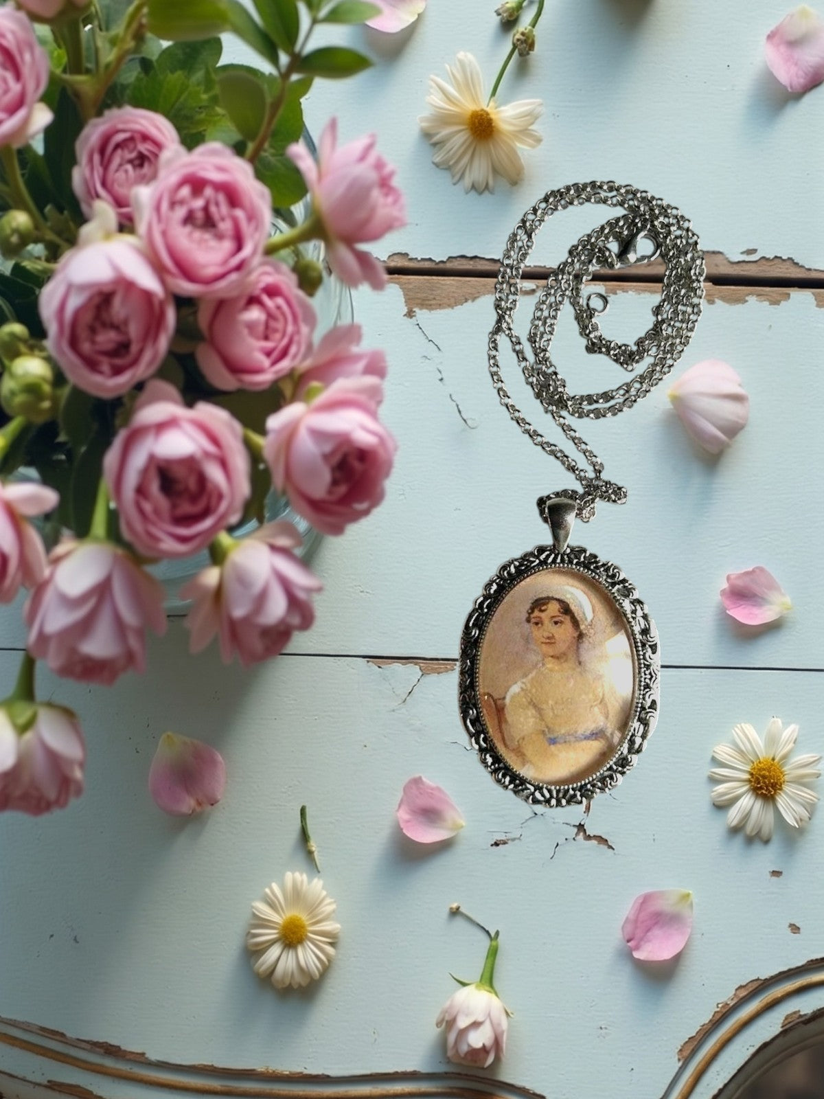 Collana artigianale con ritratto di Jane Austen su ciondolo ovale argento, posata su tavolo, Italia