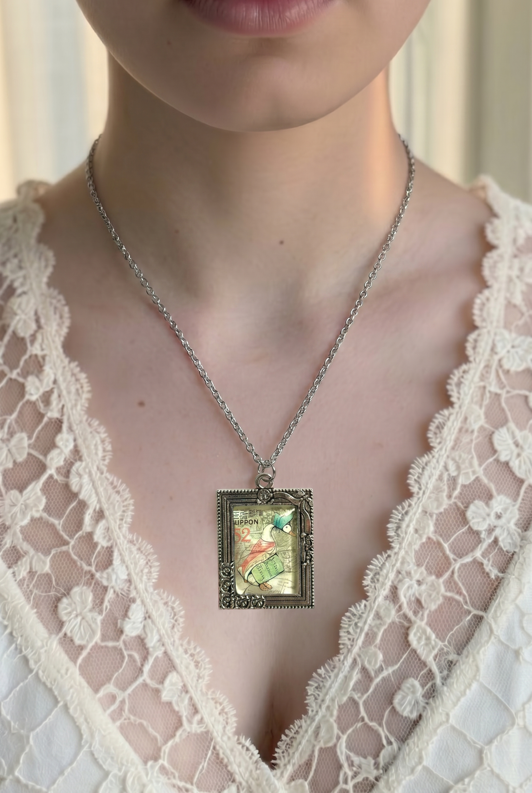 Collana con francobollo giapponese di Jemima, l'anatra di Beatrix Potter con cuffietta e scialle, cornice rettangolare in argento con rose, indossata