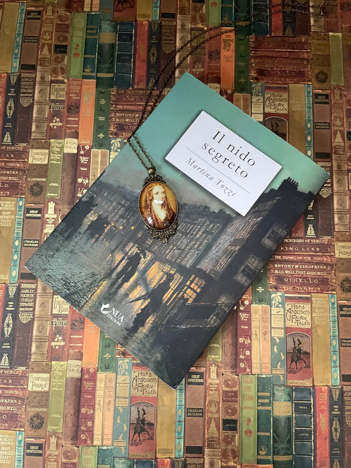 Collana Mary Shelley in bronzo appoggiata su un libro, sfondo di dorsi di libri antichi