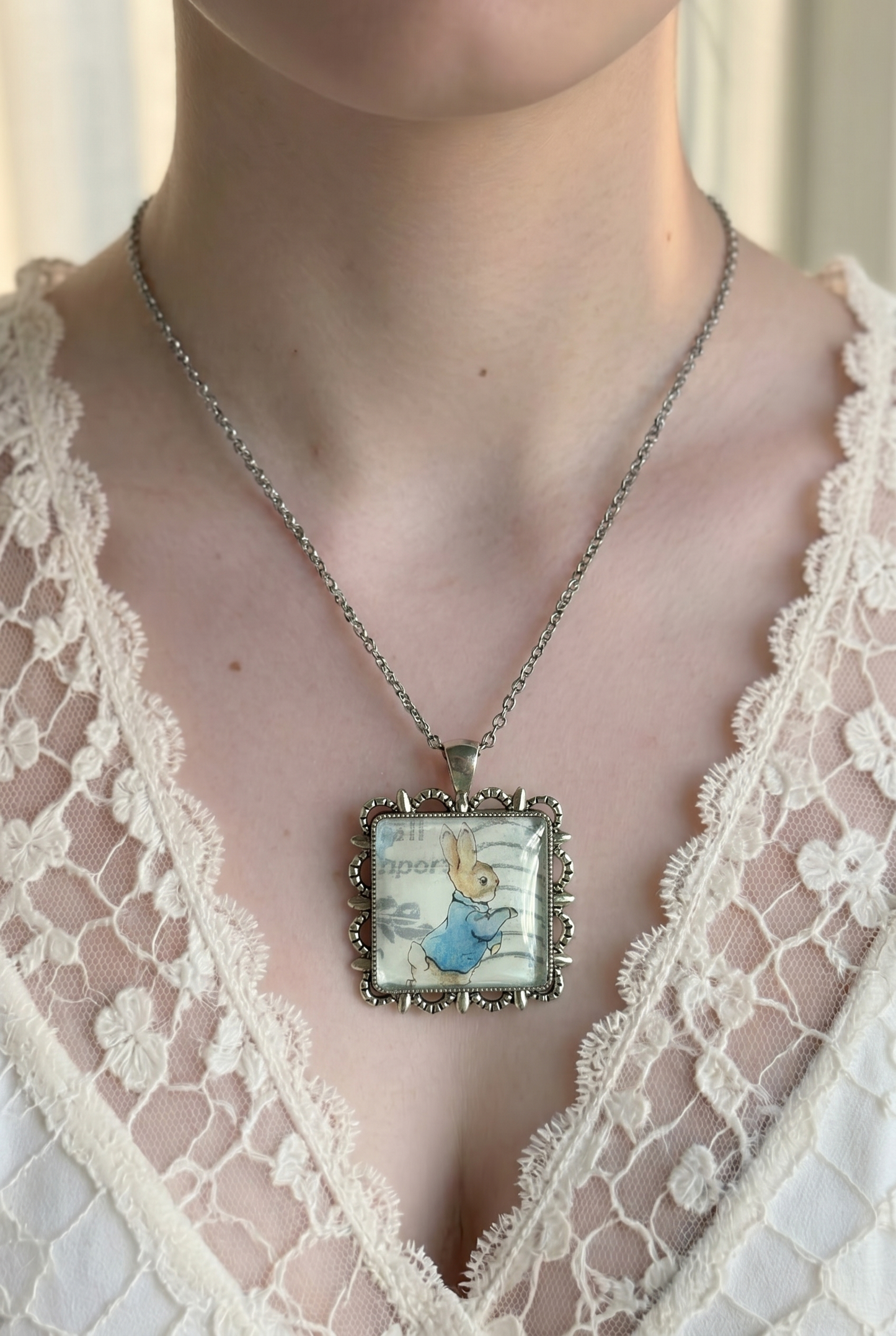 Collana con francobollo giapponese di Peter Rabbit di Beatrix Potter, coniglio in giacca azzurra, cornice quadrata in argento a smerli, indossata 
