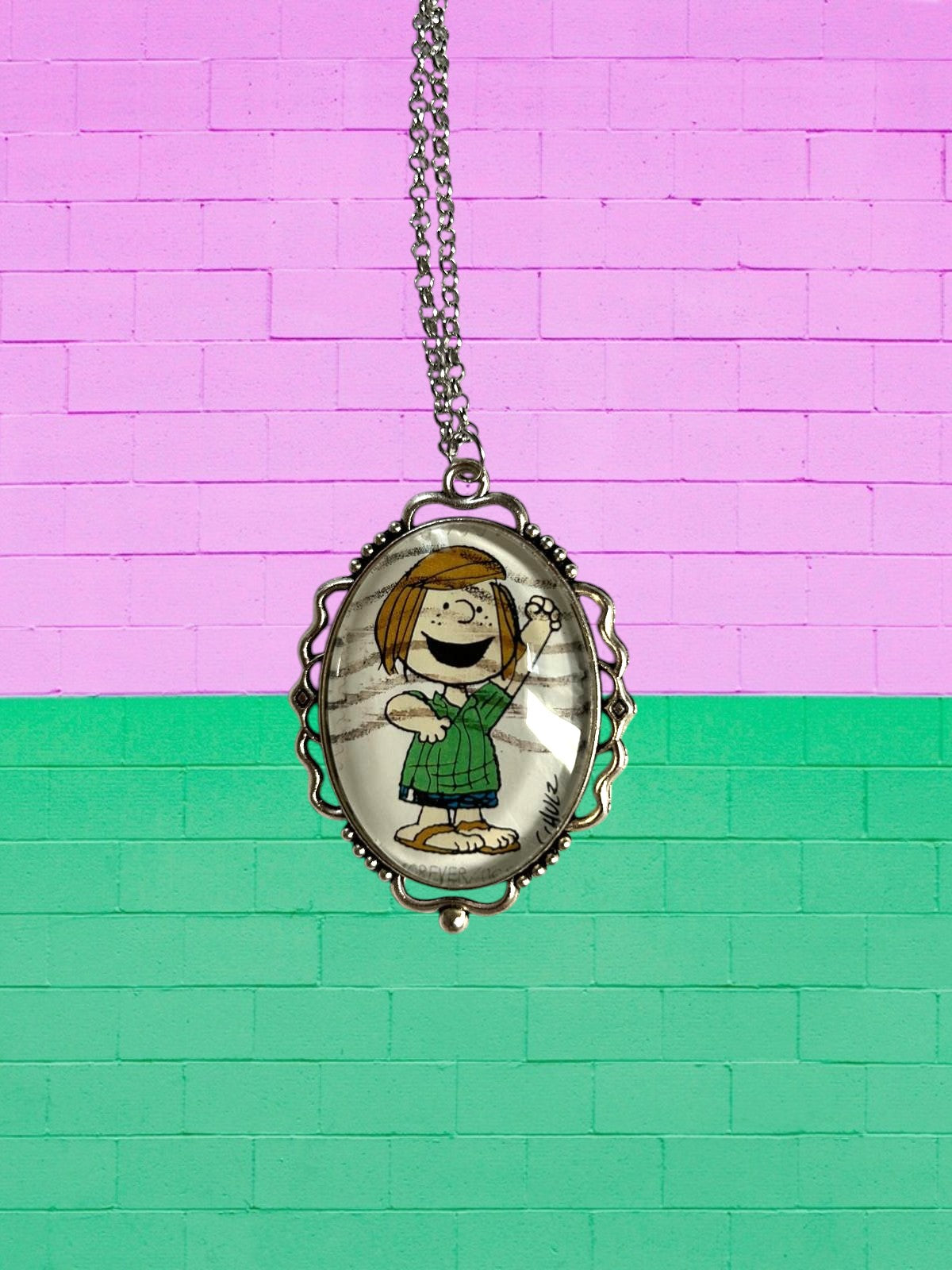 Collana artigianale italiana con francobollo di Piperita Patty, ciondolo ovale argentato su muro rosa e verde