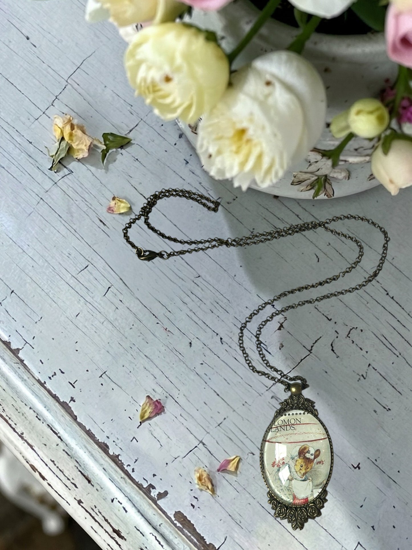 Collana con francobollo del sarto di Gloucester di Beatrix Potter, topolina con cuffietta, cornice ovale in bronzo a filigrana e rose sul tavolo con vaso di fiori, artigianato, Italia