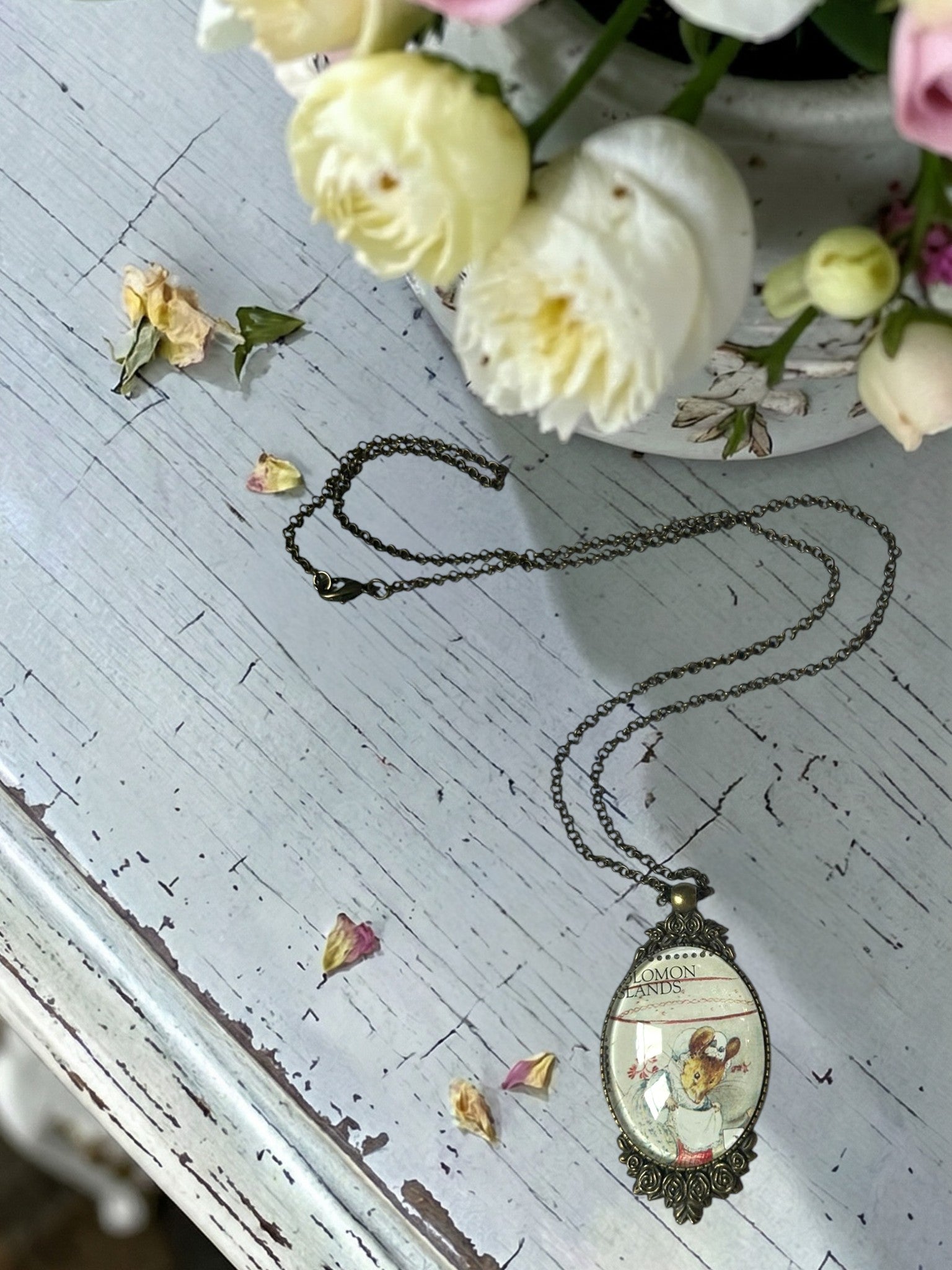 Collana con francobollo del sarto di Gloucester di Beatrix Potter, topolina con cuffietta, cornice ovale in bronzo a filigrana e rose sul tavolo con vaso di fiori, artigianato, Italia