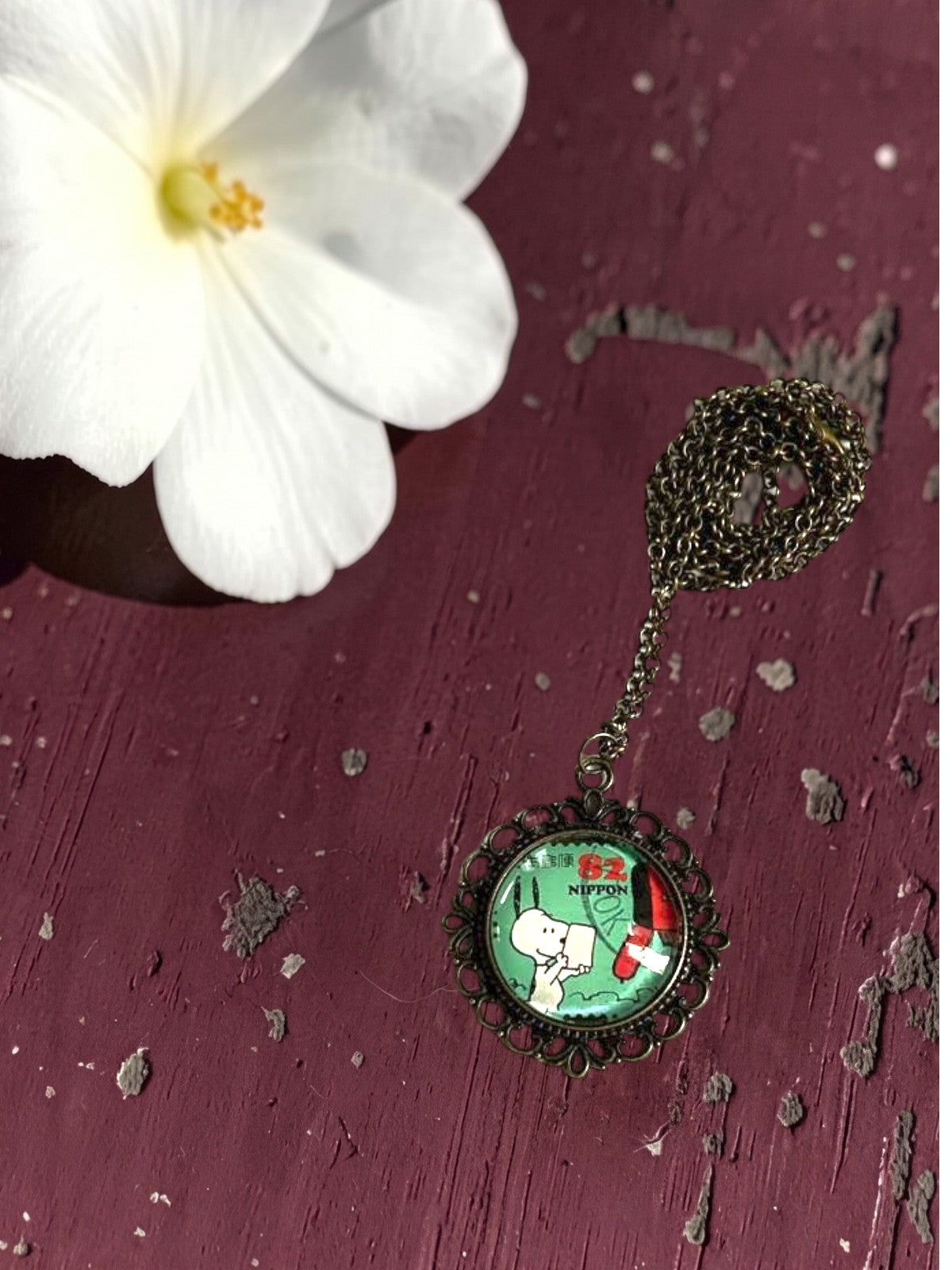 Ciondolo tondo artigianale italiano con francobollo Snoopy dei Peanuts su tavolo bordeaux, cornice bronzo