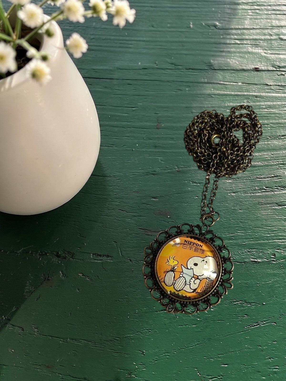 Ciondolo tondo artigianale italiano con francobollo Snoopy e Woodstock dei Peanuts su tavolo verde, cornice bronzo