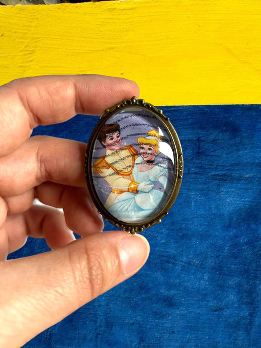 Spilla artigianale italiana con francobollo di Cenerentola e il Principe in mano su muro colorato