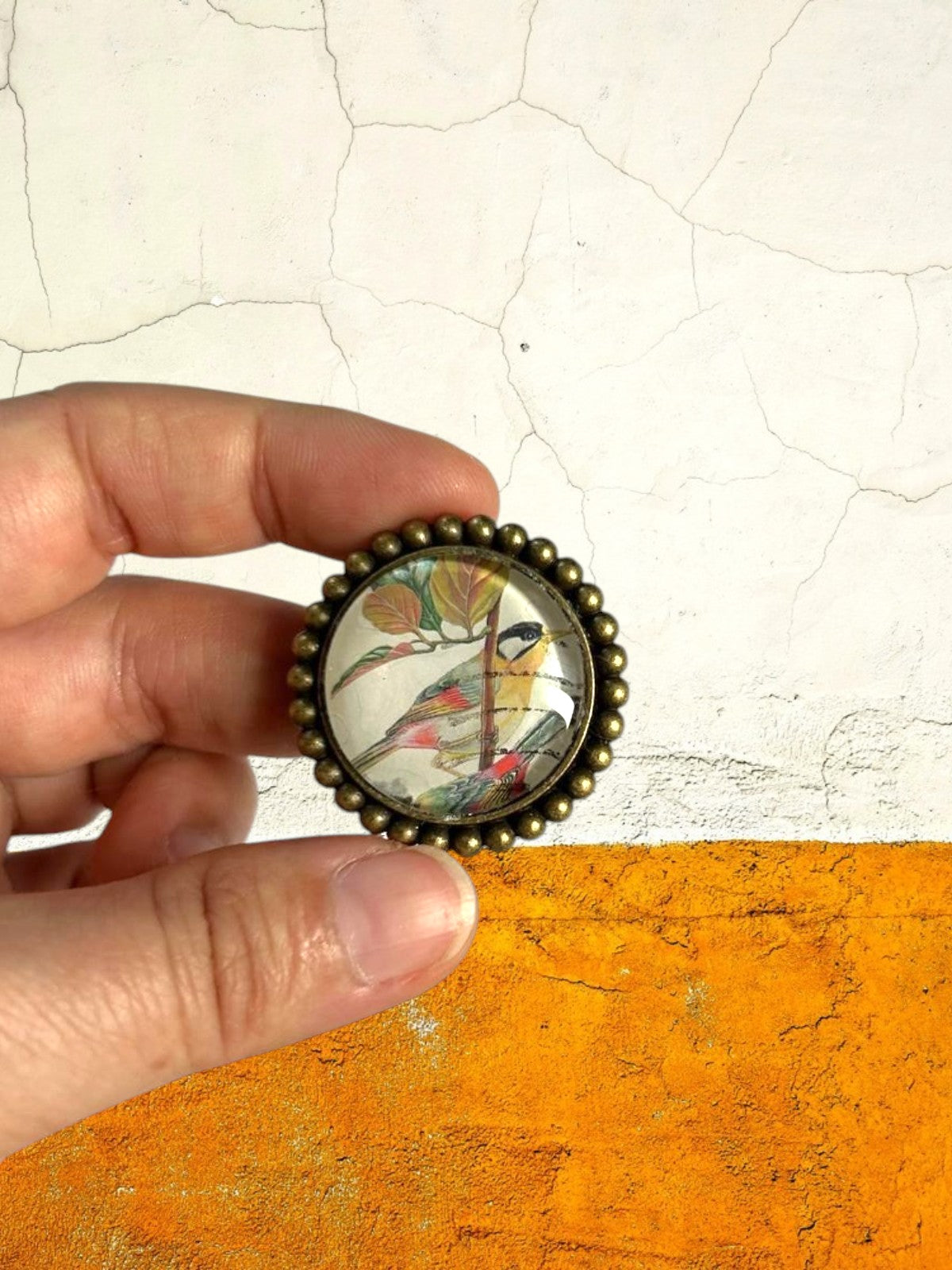 Spilla uccellini con francobollo malese tenuta in mano, creazione artigianale italiana, muro bianco