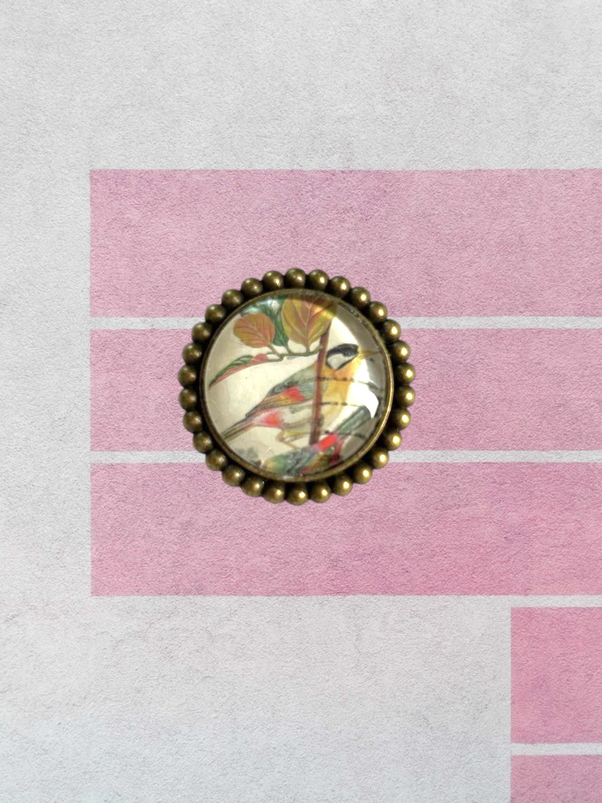 Spilla artigianale italiana con francobollo di uccellini della Malesia su sfondo rosa geometrico